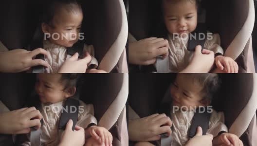 母亲双手合拢，正在给汽车座椅上的婴儿系安全带。高清在线视频素材下载