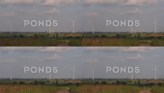 风力涡轮机高耸在农田上方，农民种植庄稼并照料高清在线视频素材下载